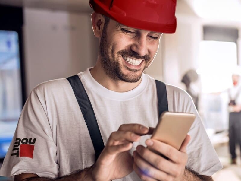 Uśmiechnięty wykonawca w kasku sprawdza zamówienie w telefonie