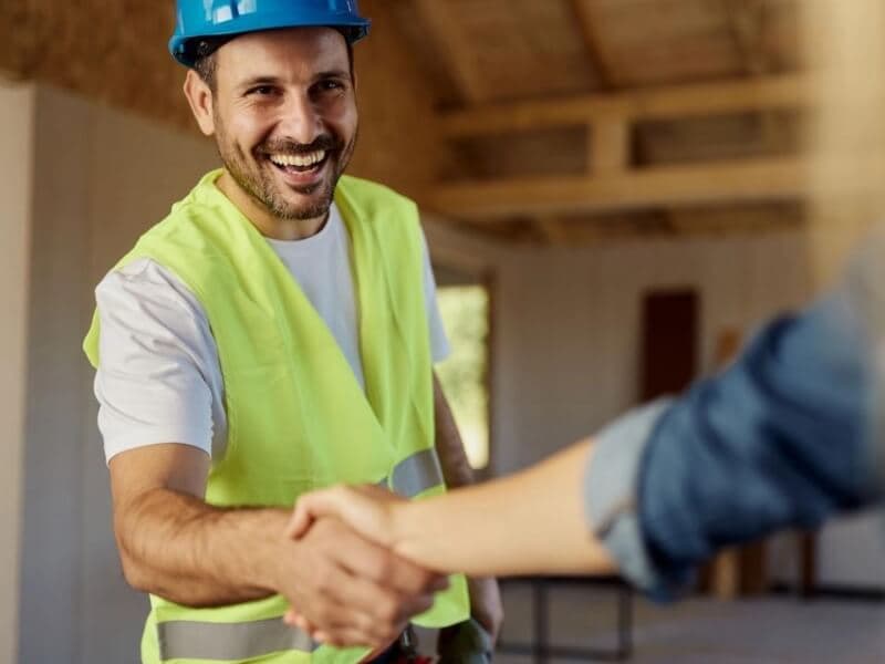 Wykonawca w kasku i kamizelce odblaskowej podaje rękę partnerowi na budowie